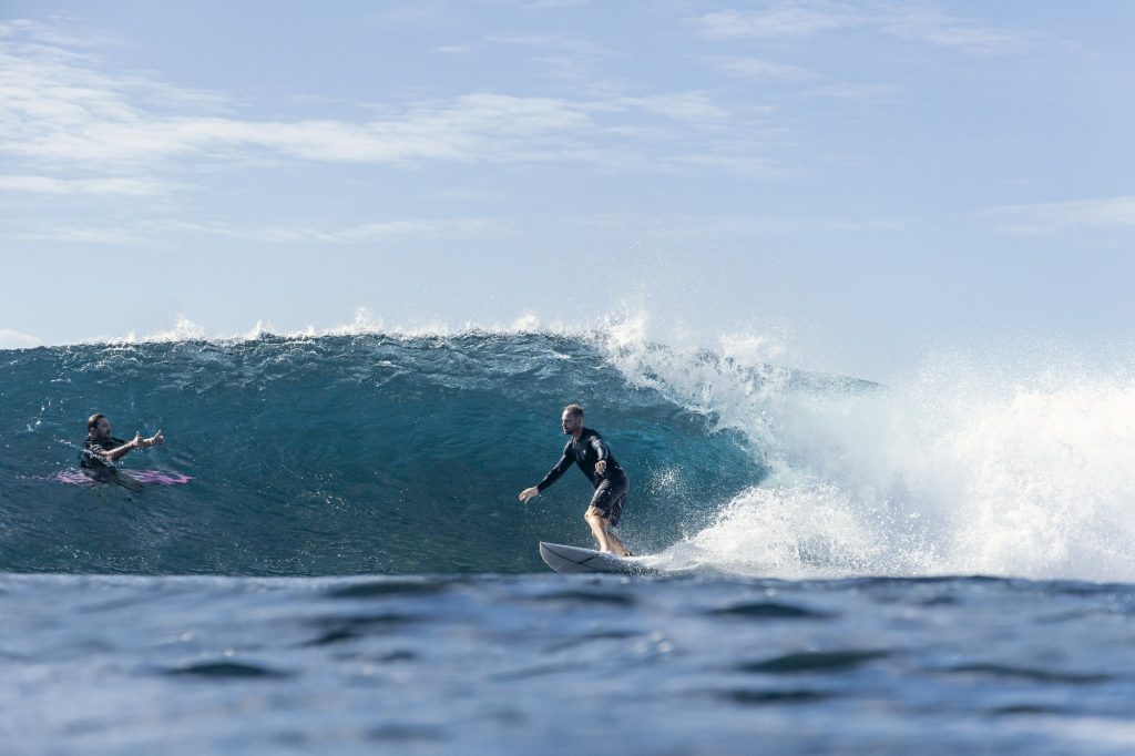 Surf coach in the water beside a student riding a wave