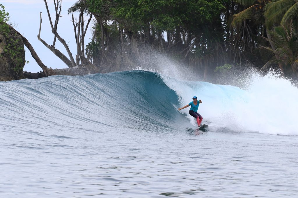 Surfer riding a clean green wave with a jungle backdrop